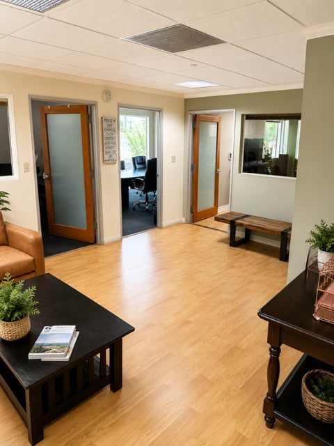Modern office waiting room with wood flooring, wooden doors, black tables, plants, and seating area