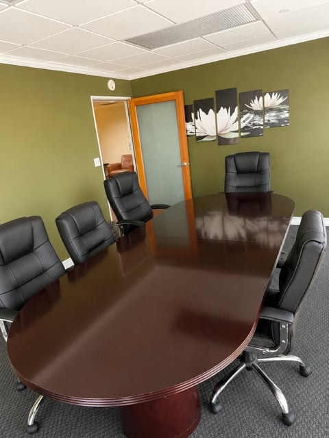 Modern conference room with oval dark wood table, black leather chairs, green walls, white ceiling panels, and decorative flower artwork