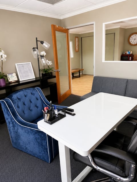 Modern office interior with white desk, blue chair, black furniture, wooden door, mirror, and potted plant