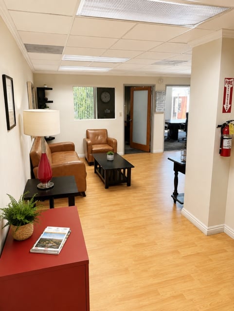 Modern office waiting room with brown leather chairs, wood flooring, red table, and neutral wall decor
