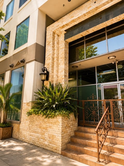 Modern brick building entrance with glass doors, ornate iron railings, potted plants, and decorative outdoor lighting
