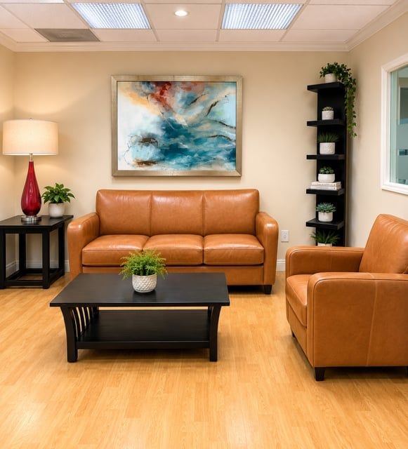 Modern living room with tan walls, orange leather sofa and armchair, black coffee table, abstract blue artwork, and wood flooring