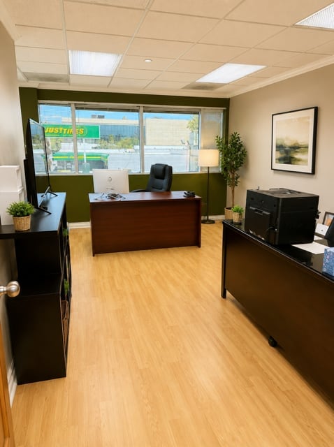 Modern office reception area with wooden desk, black cabinets, and large windows overlooking a parking lot
